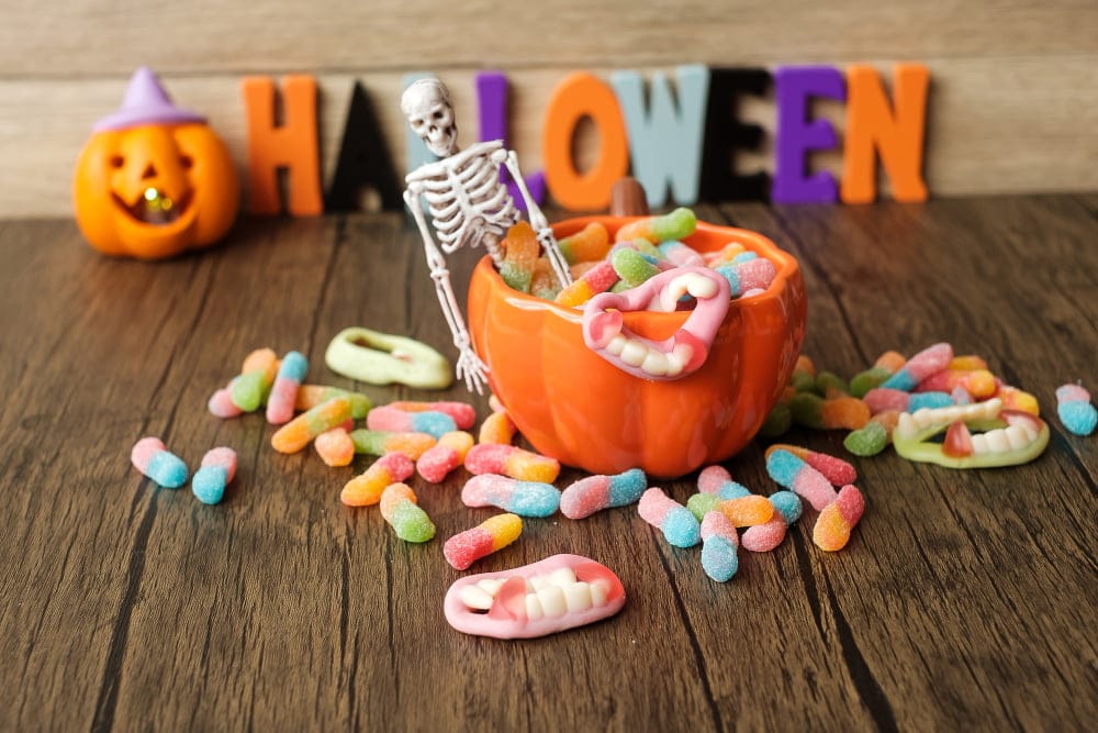 Decoración de Halloween con dulces coloridos en un recipiente con forma de calabaza, un esqueleto pequeño y dentaduras de caramelo, destacando la importancia del cuidado dental durante las festividades.